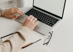 A clean and modern workspace featuring a laptop, houseplant, and notebook.
